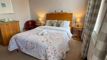 A hotel room with a large bed, a wooden dresser, a chair, and a nightstand with lamps.