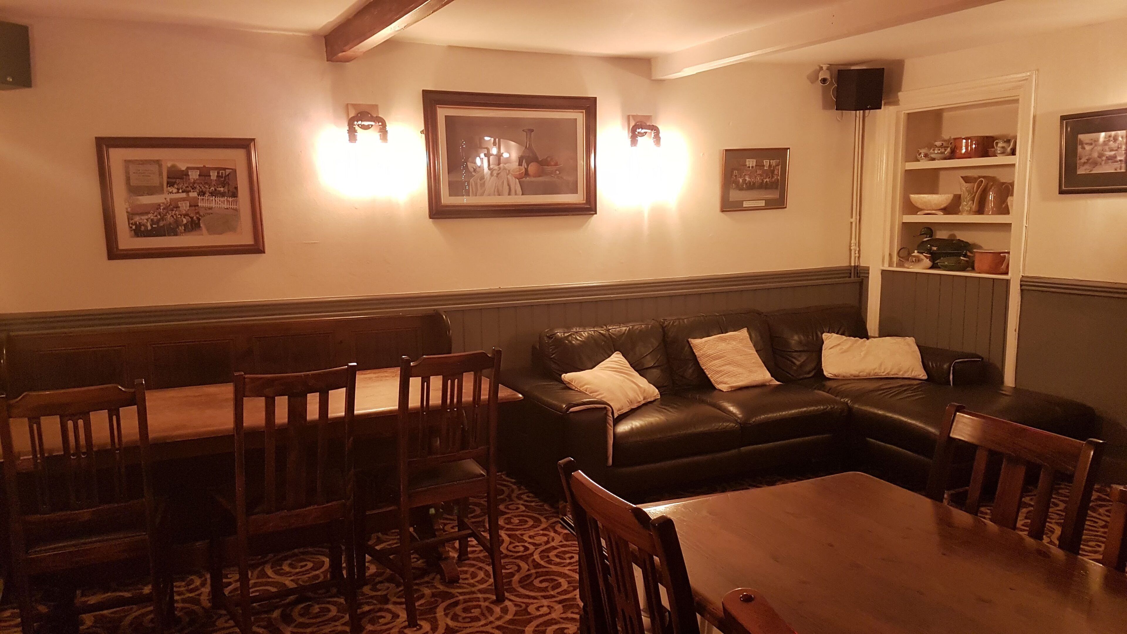 Un comedor con una mesa y sillas de madera, un sofá de cuero negro y cuadros en las paredes.