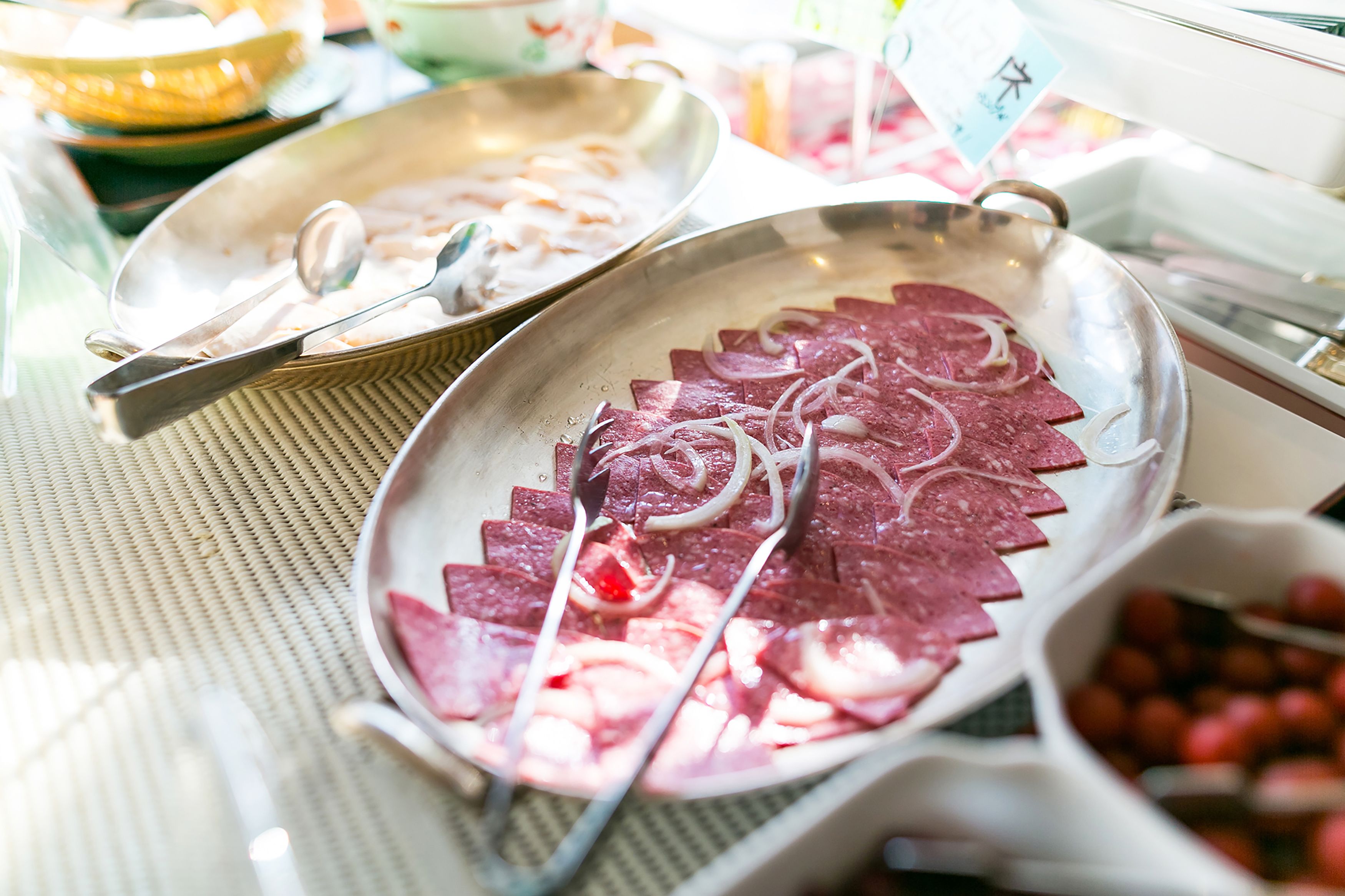 Ein Esstisch mit verschiedenen Speisen, darunter geschnittenes Fleisch und Zwiebeln, sowie eine Schüssel mit Kirschen.