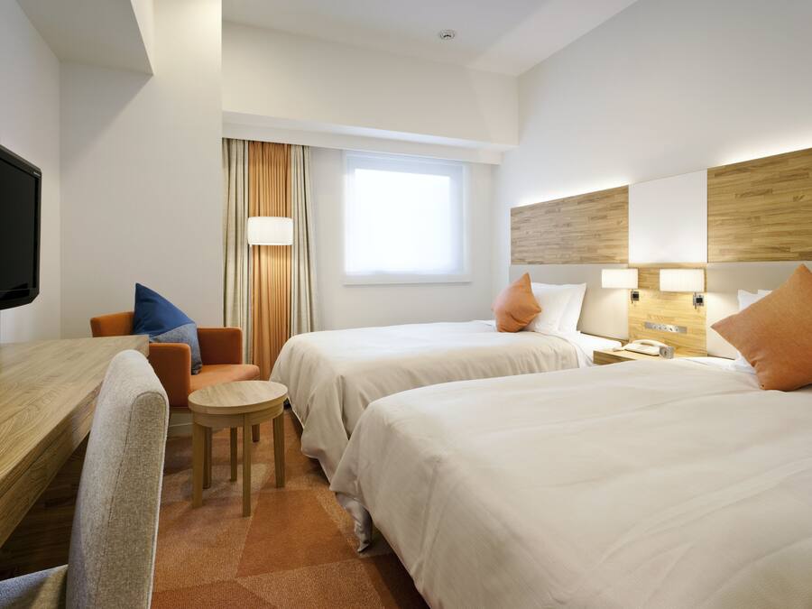 A hotel room with two beds, a desk, a chair, a television, and a window with curtains.