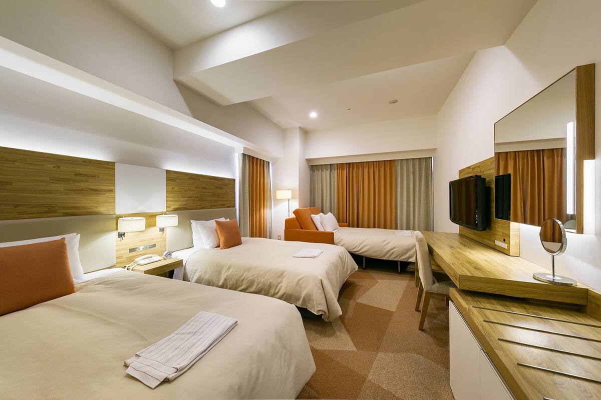 A hotel room with two beds, a desk, a mirror, a television, and a lamp.