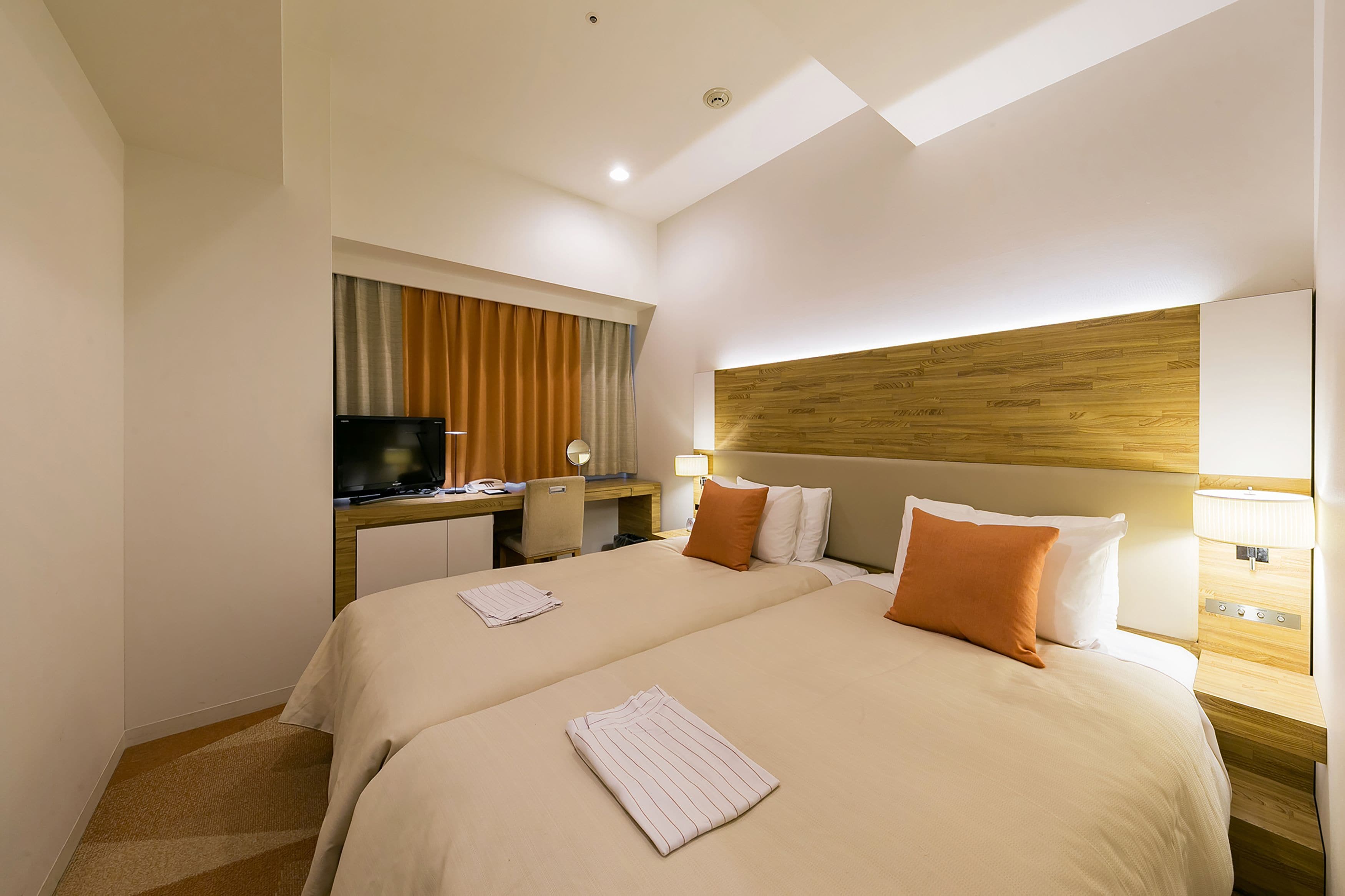 Habitación de hotel con dos camas, un escritorio con televisor y un cabecero de madera.
