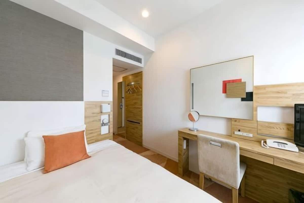 A hotel room with a bed, a desk, a chair, a mirror, and a television.
