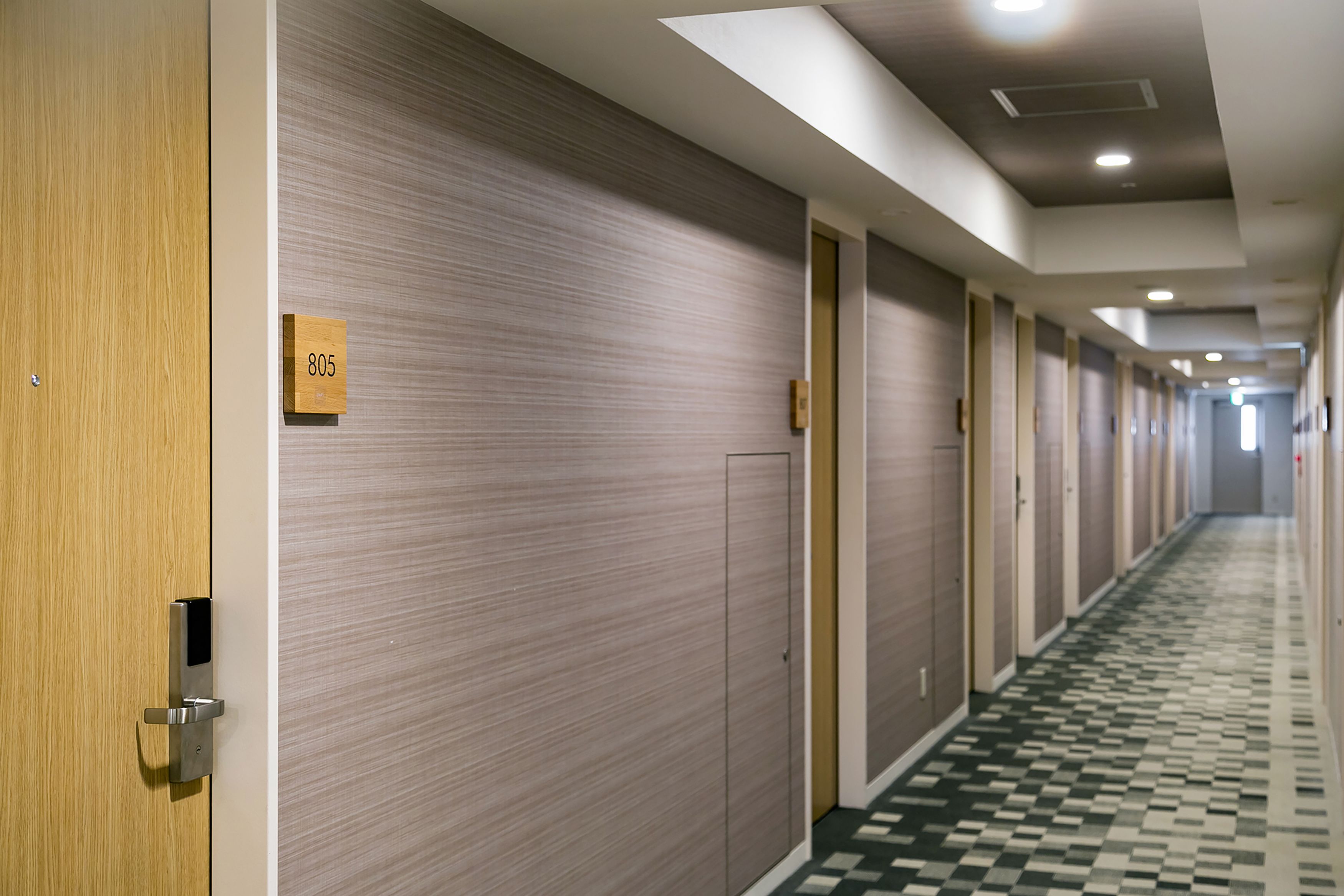 A hotel corridor with a checkered floor, wooden doors, and a number sign on one door.
