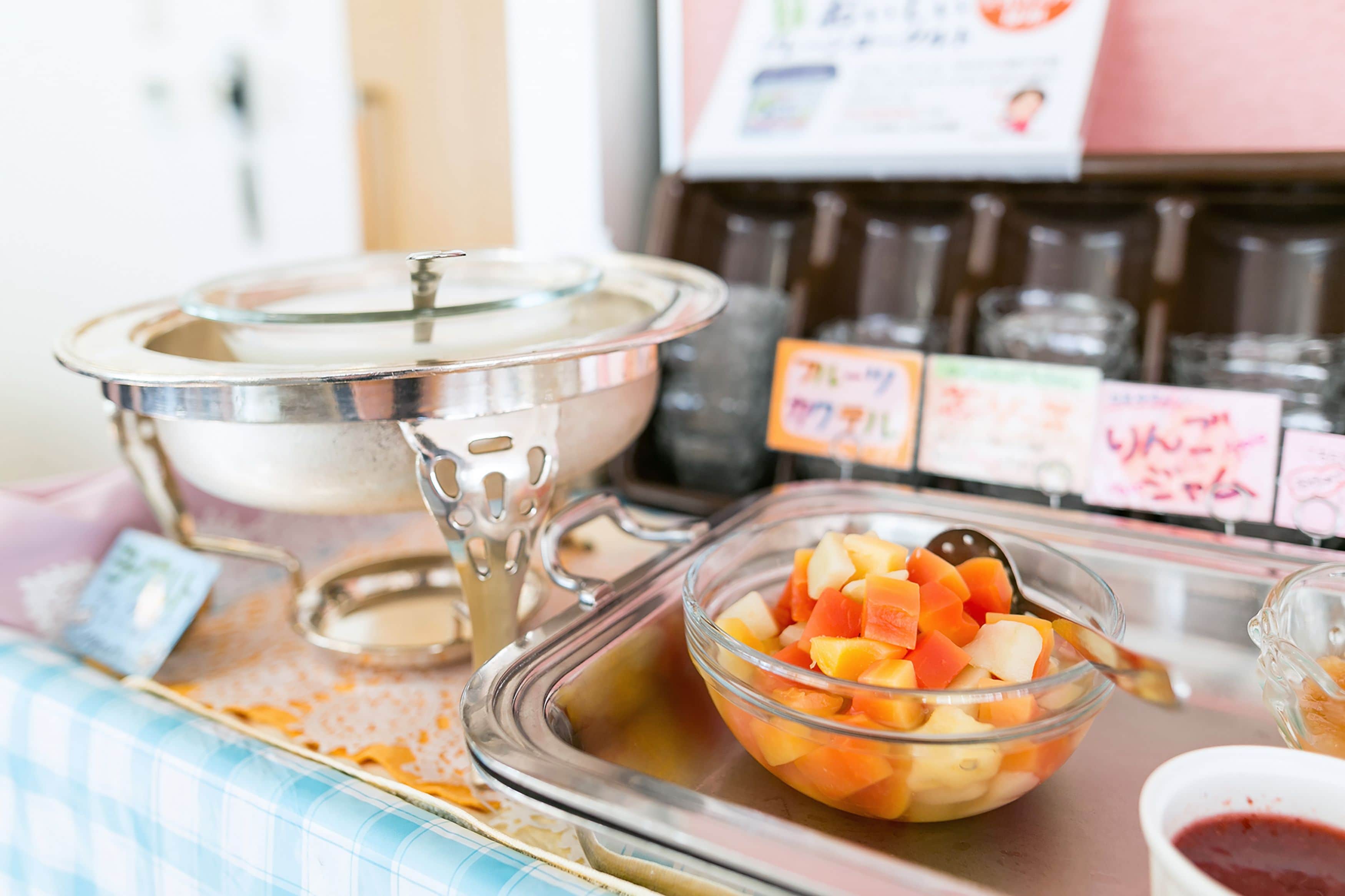 Ein reichhaltiges Buffet mit verschiedenen Speisen, darunter eine Schale Obstsalat und ein abgedecktes Gericht, vermutlich mit Suppe oder Salat.