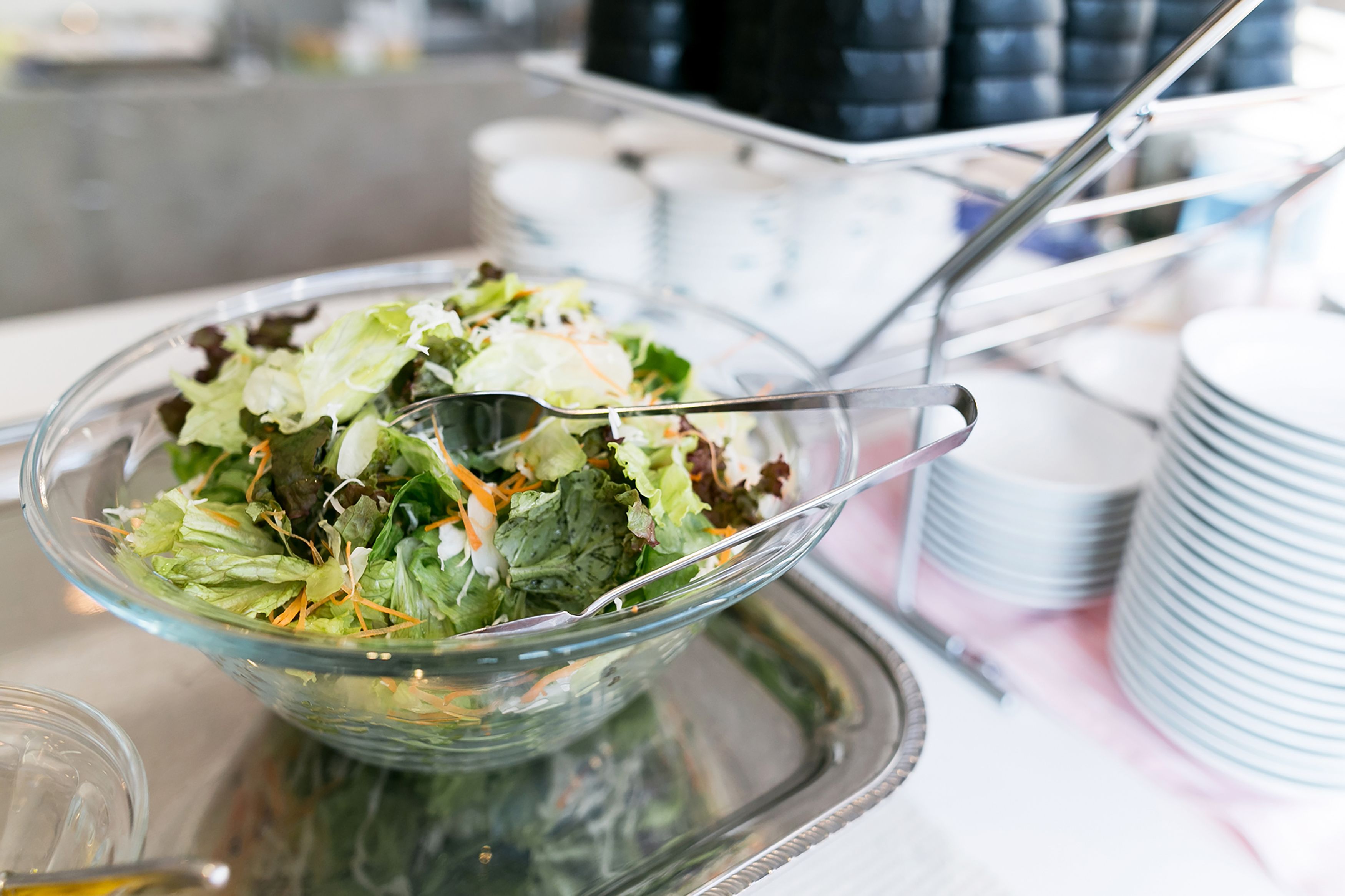 A clear glass bowl filled with a salad on a tray, accompanied by a spoon.