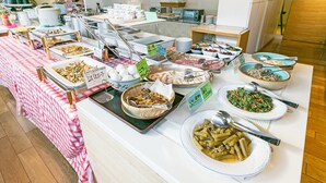 A buffet with various dishes, including meats, vegetables, and desserts, arranged on a table with a checkered tablecloth.