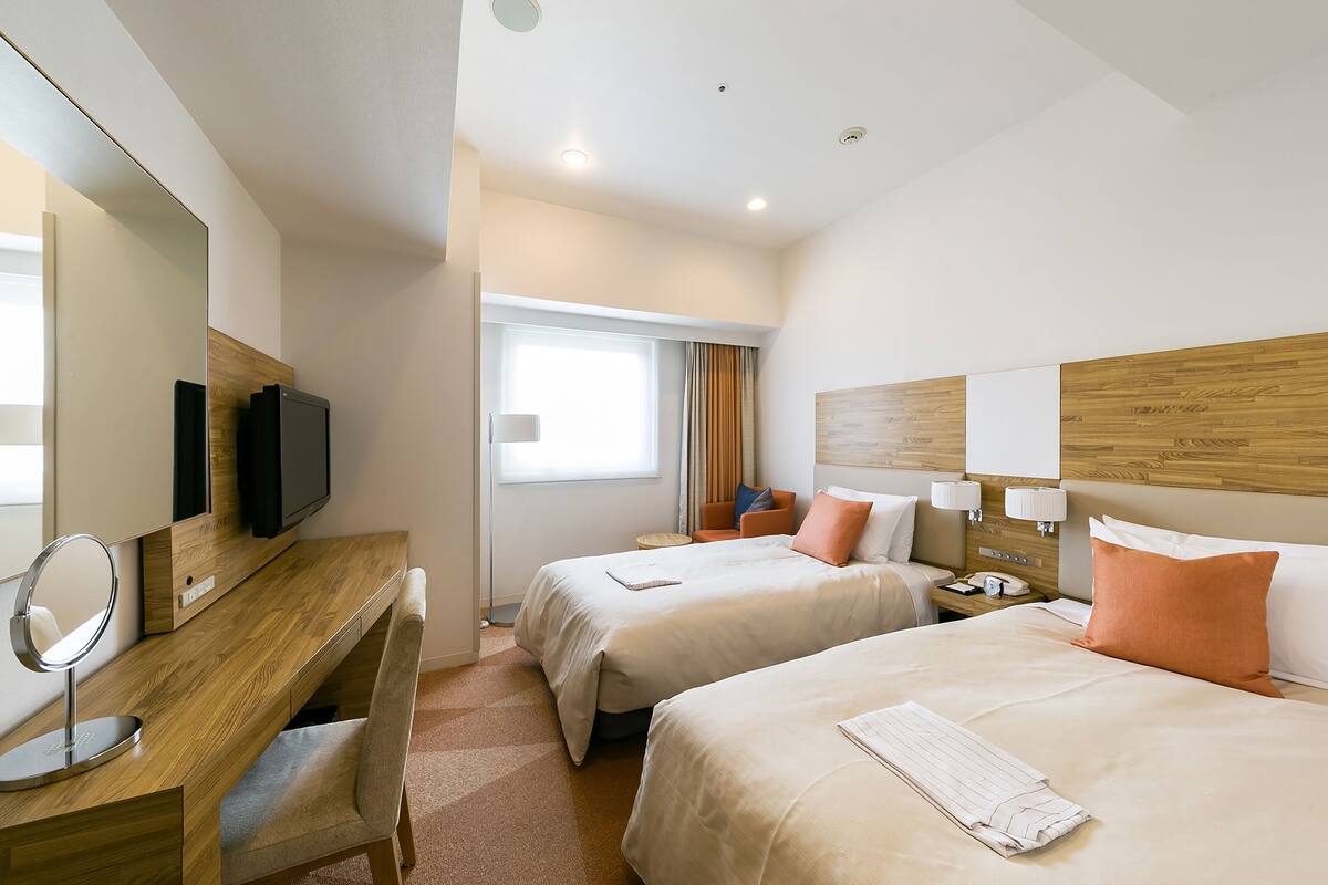 A hotel room with two beds, a desk with a mirror, a TV, and a window with curtains.