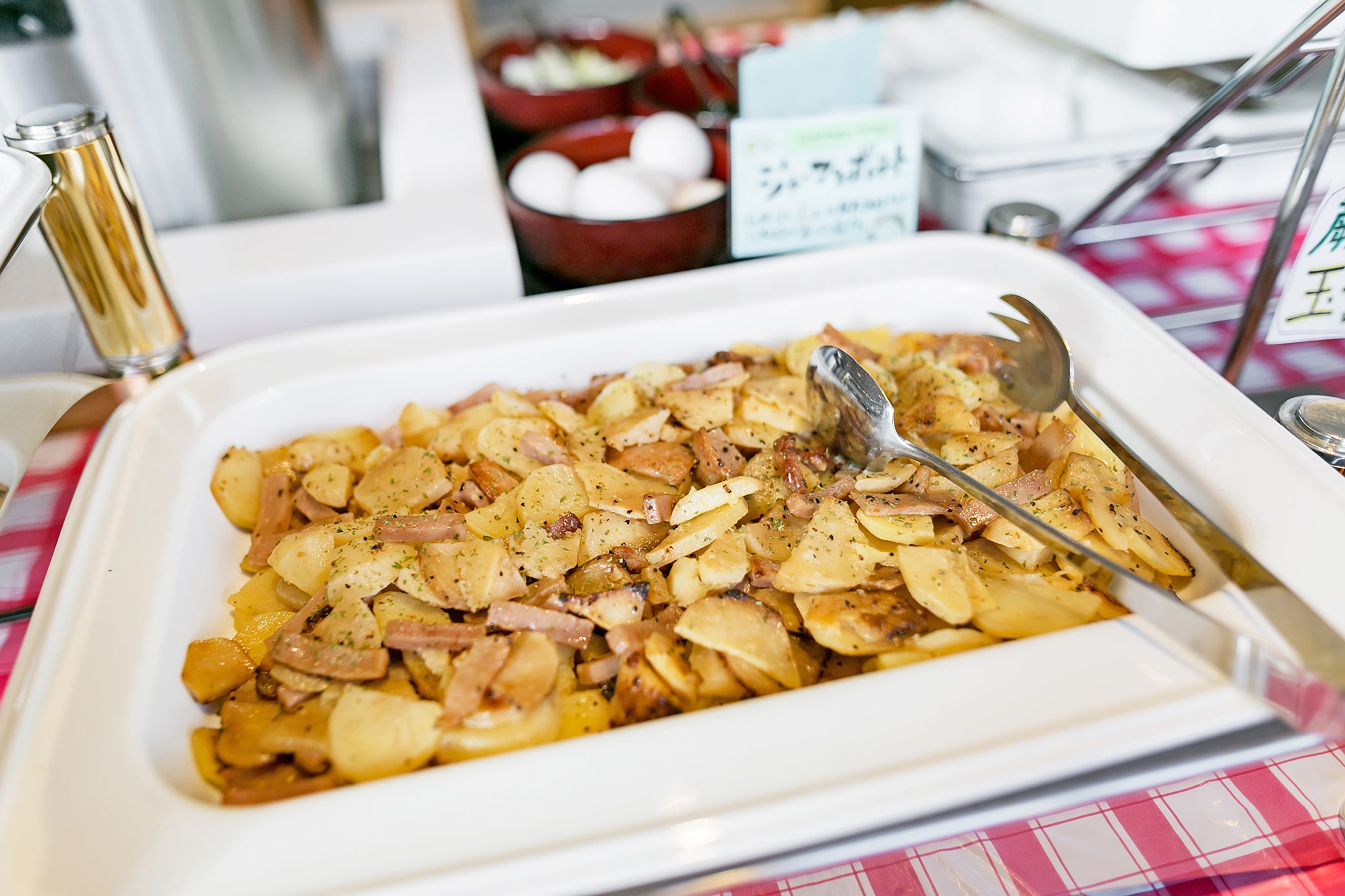Une table de buffet avec un plat de pommes de terre et de lardons.