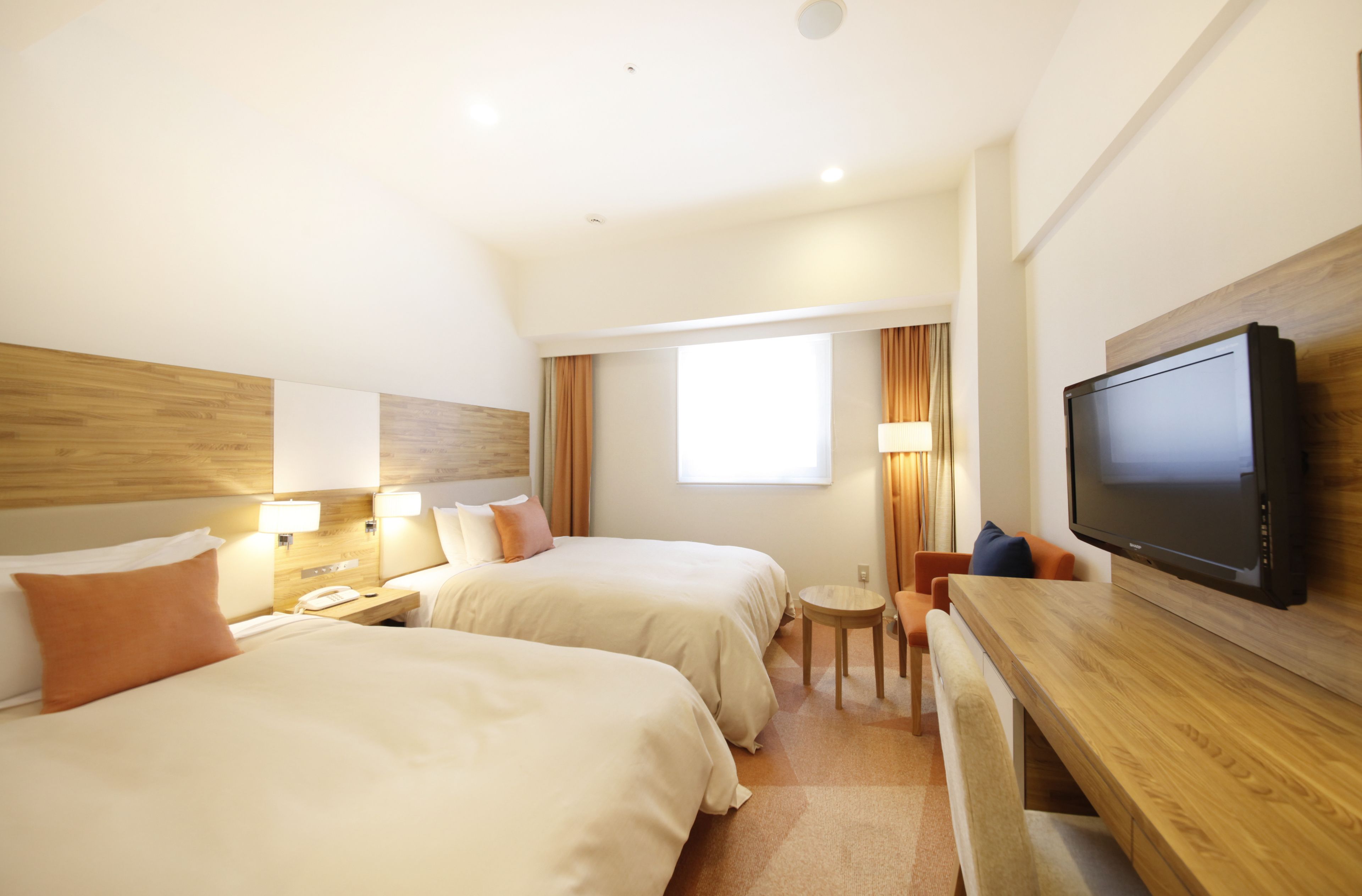 Una habitación de hotel con dos camas, televisor, escritorio y una mesita.