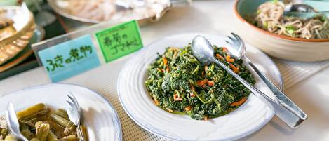 A table with various dishes, including a plate of greens and a bowl of noodles.