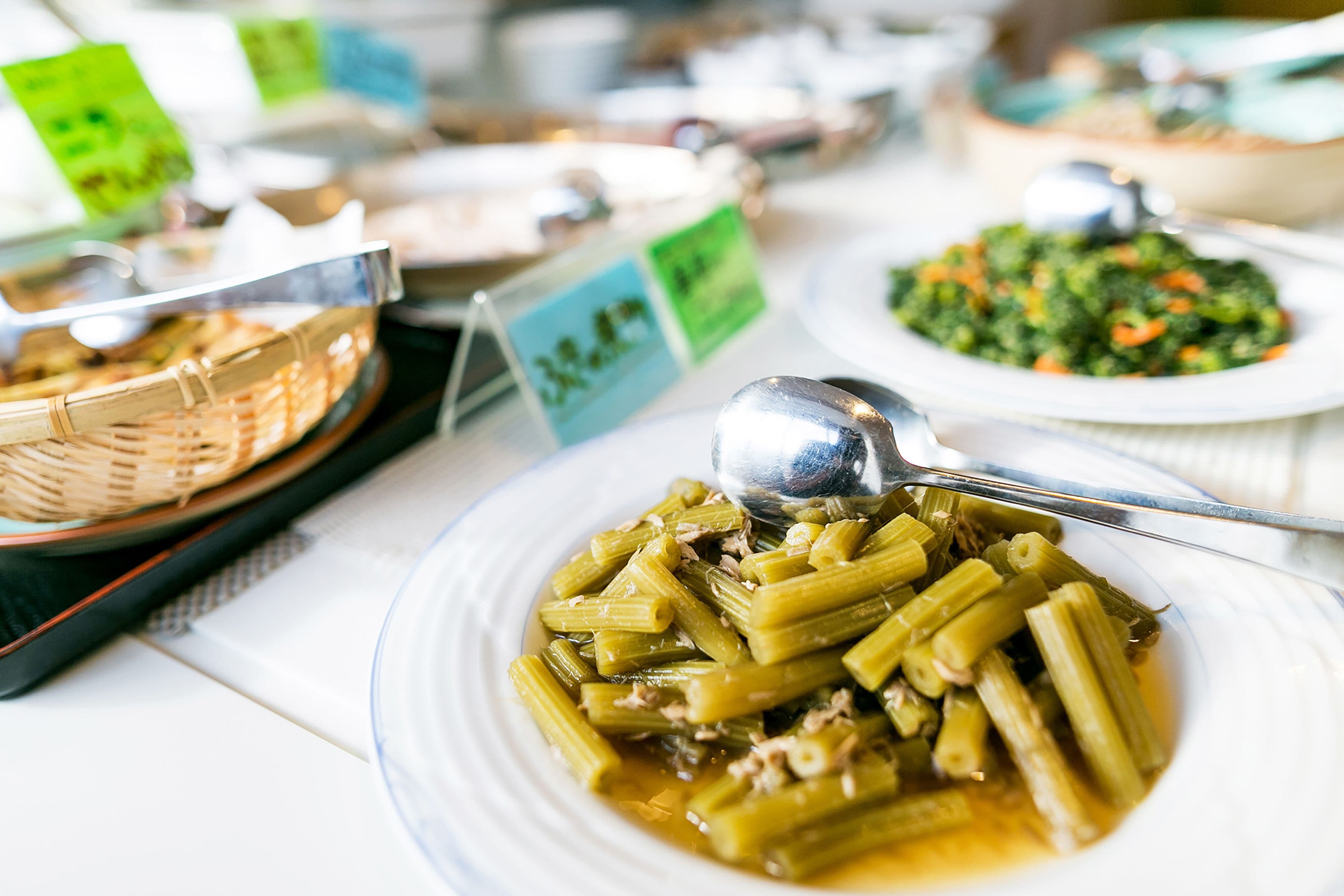 Una mesa de buffet con diversos platos, incluyendo un plato de verduras verdes y un bol de ensalada mixta.