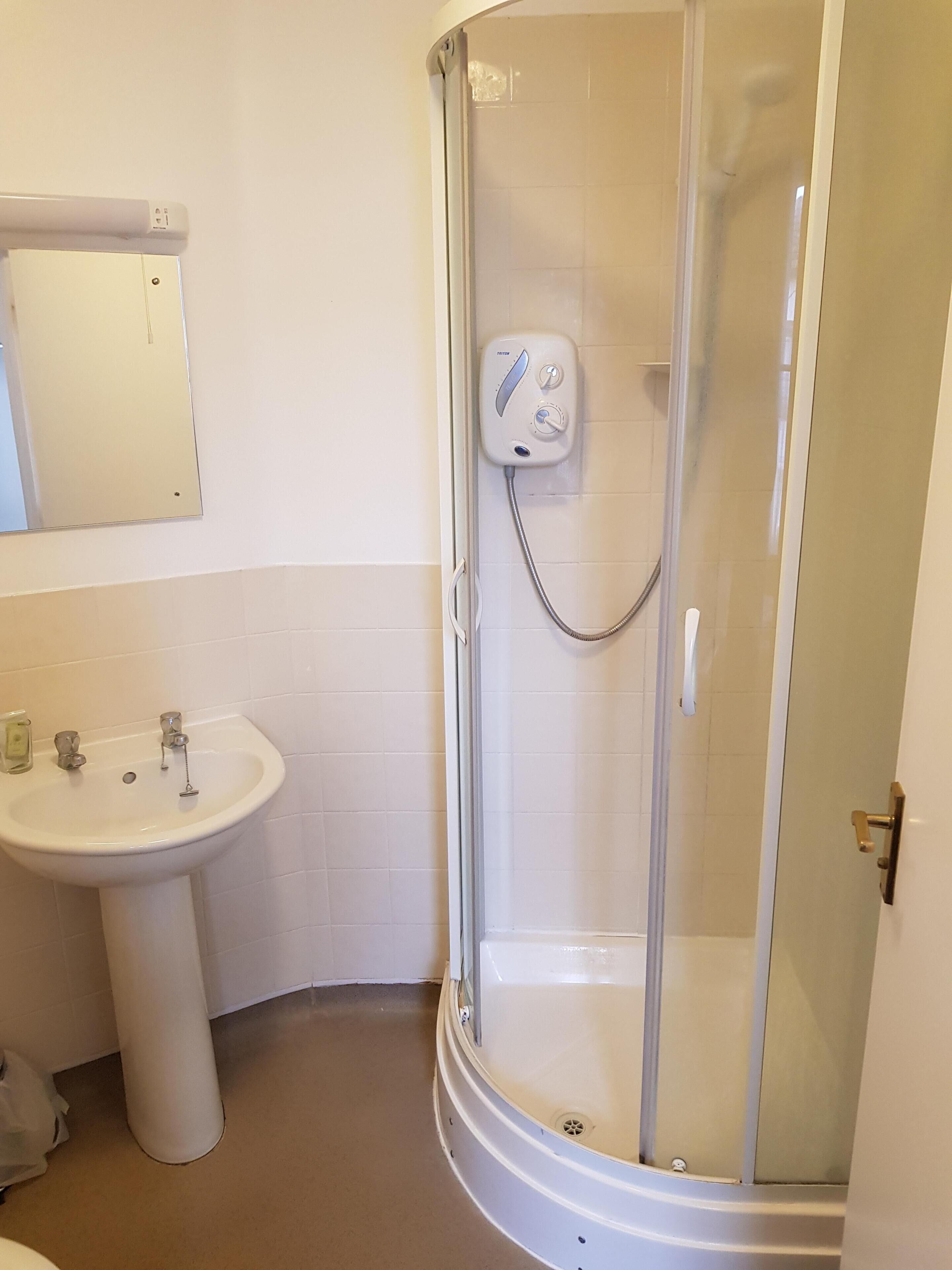 Un baño con ducha de vidrio, lavamanos pedestal y espejo montado en la pared.