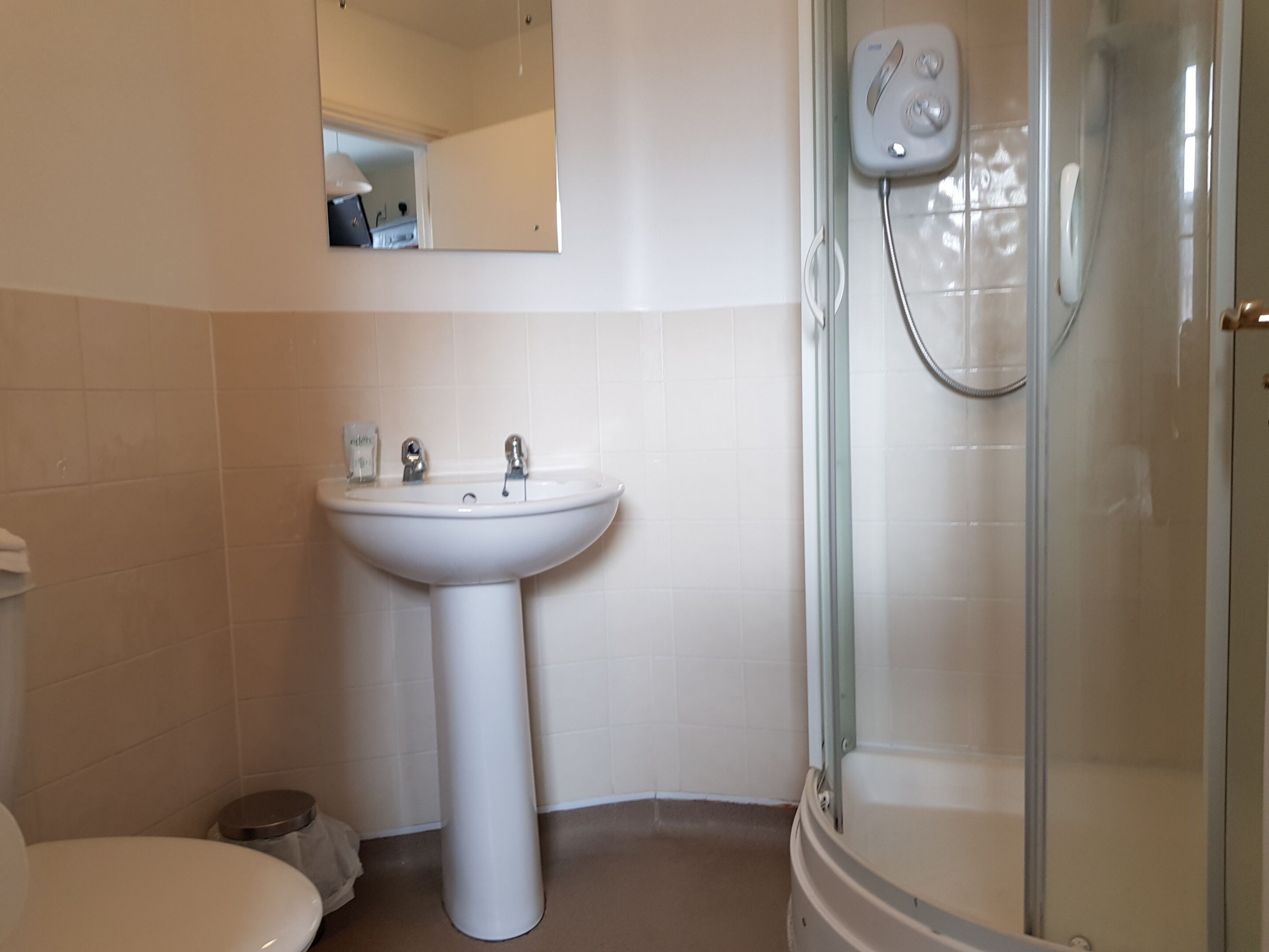 Een badkamer met een wastafel op een voetstuk, toilet en een douchecabine met glazen wanden.