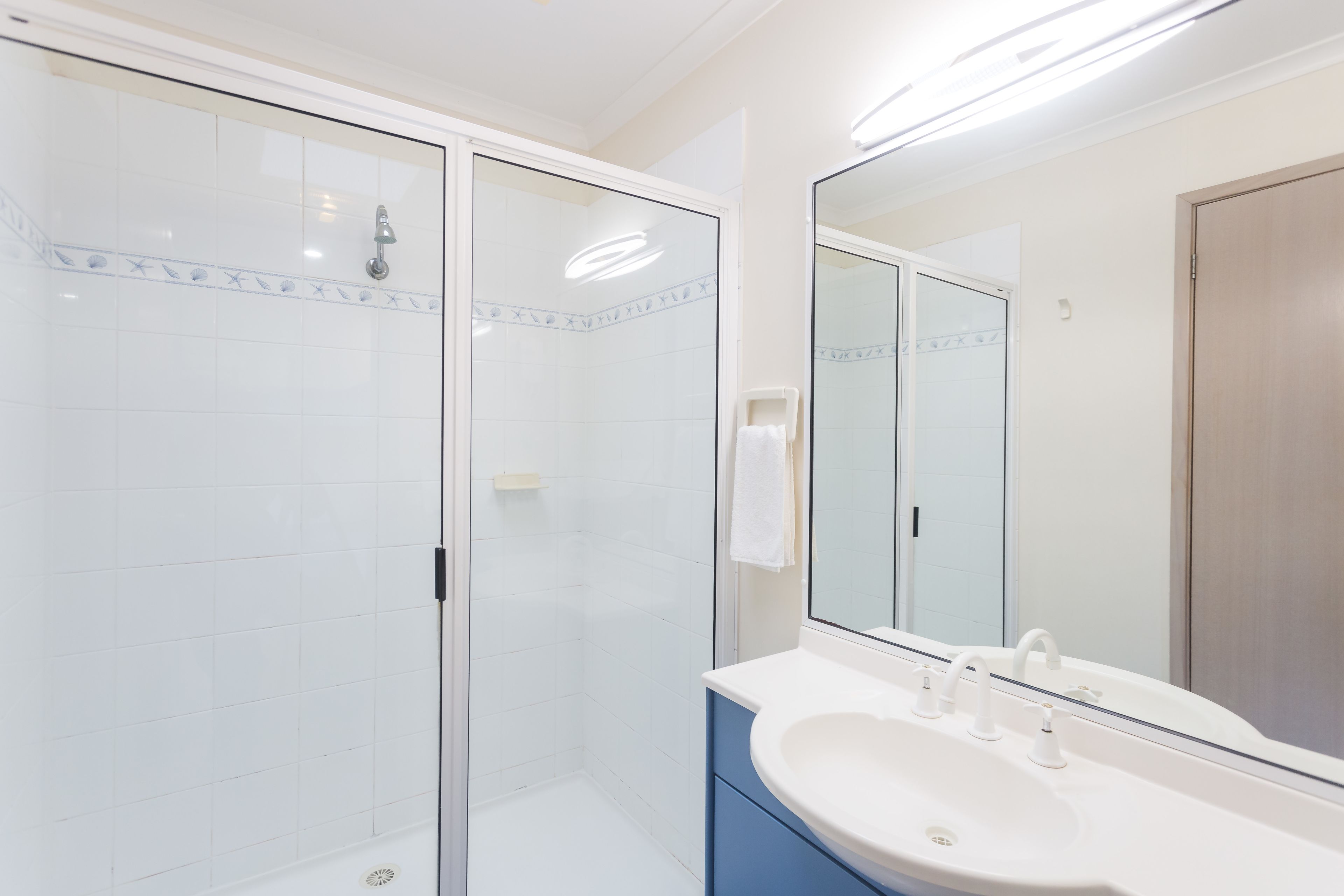 Un baño moderno con ducha envuelta en vidrio, un lavabo blanco con espejo y un mueble azul.