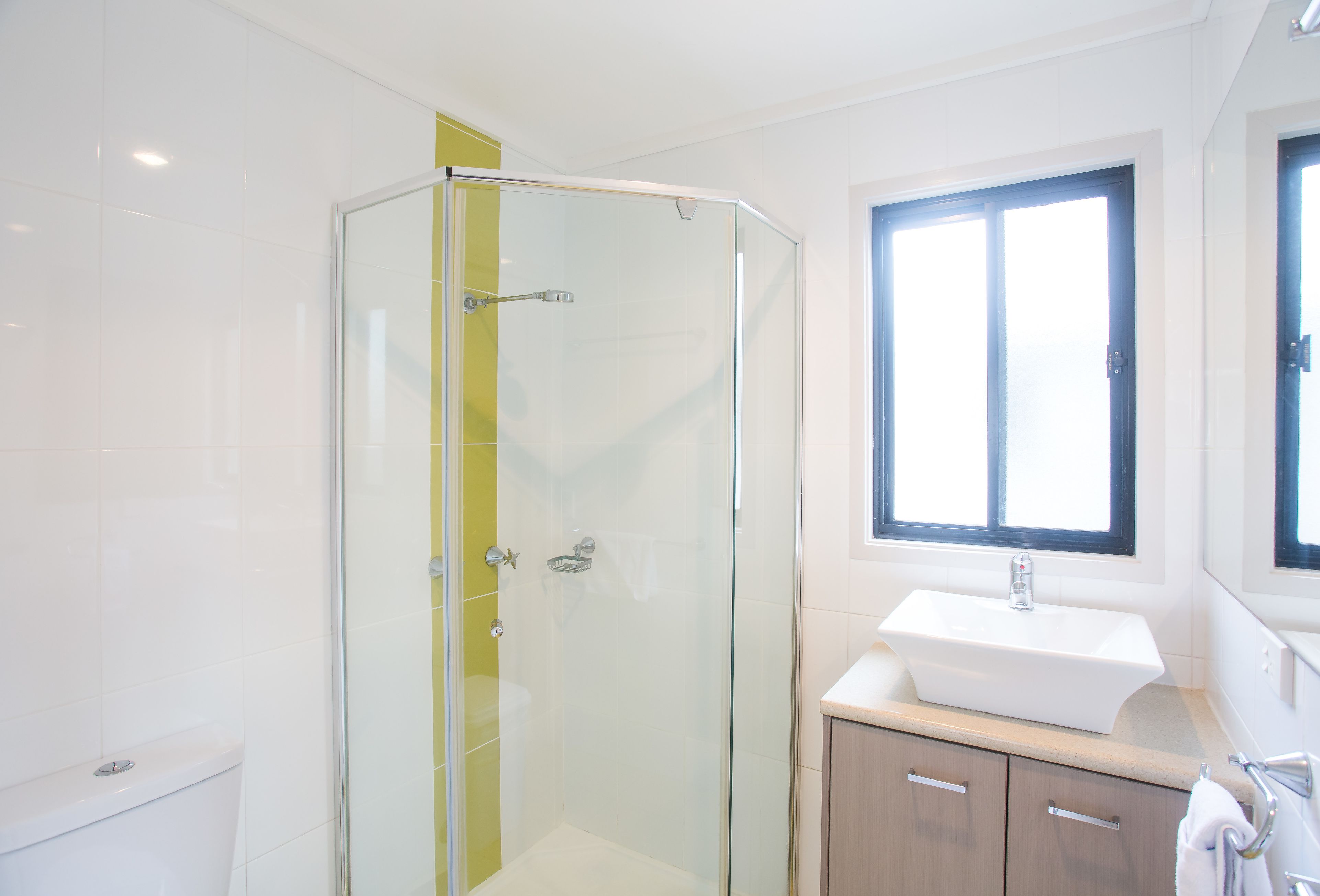 A modern bathroom with a glass shower enclosure, a sink, and a window.