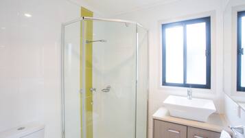 Un baño moderno con cabina de ducha de vidrio, un lavamanos y una ventana.