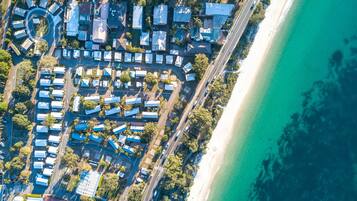 An aerial view of a coastal residential area with houses arranged in a circular pattern around a central road, adjacent to a beach.