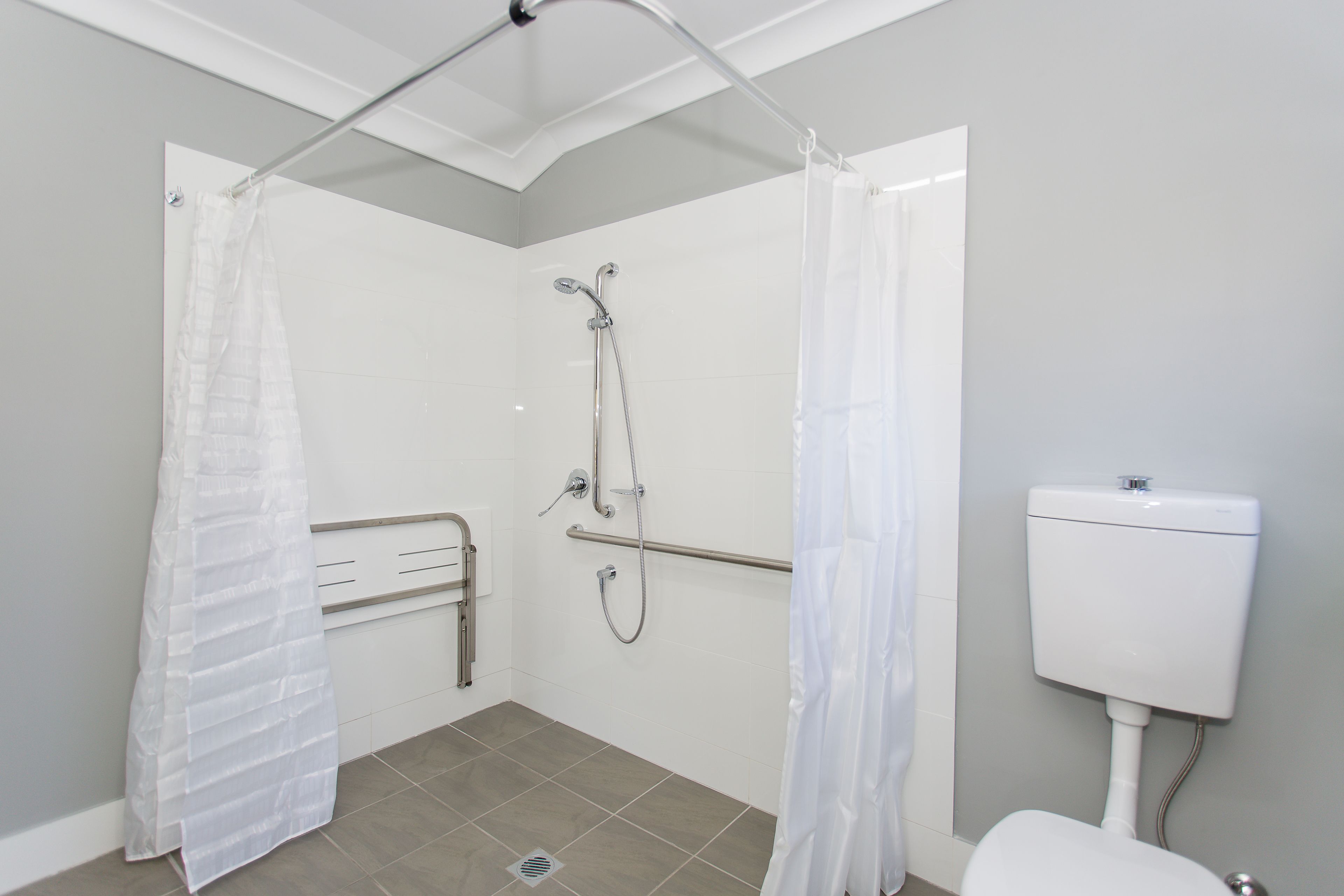 A bathroom with a shower, toilet, and grab bar.