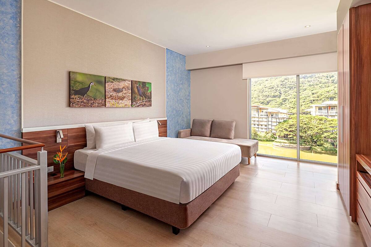 Ein modernes Hotelzimmer mit einem großen Bett, einer Sitzecke und einem Balkon mit Blick auf die umliegende Landschaft.