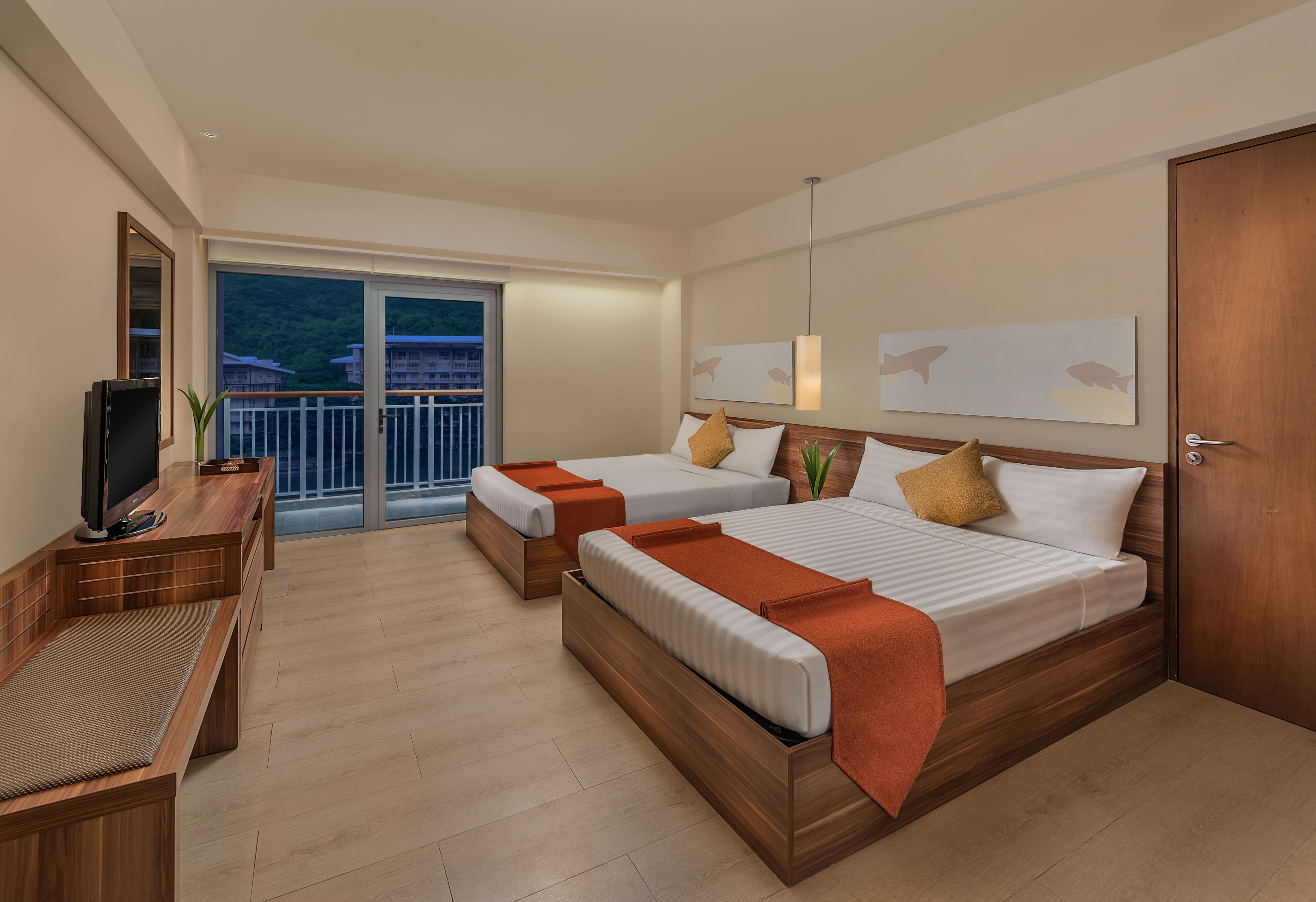 A hotel room with two beds, a TV, and a balcony with a view of buildings.