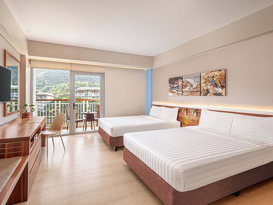 Habitación de hotel con dos camas, un escritorio y balcón con vista a las montañas.