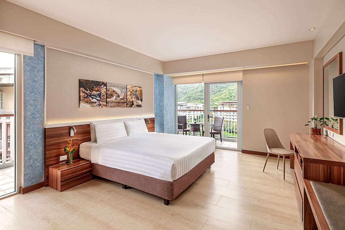 Ein modernes Hotelzimmer mit einem großen Bett, einem Schreibtisch und einem Balkon mit Sitzgelegenheit.
