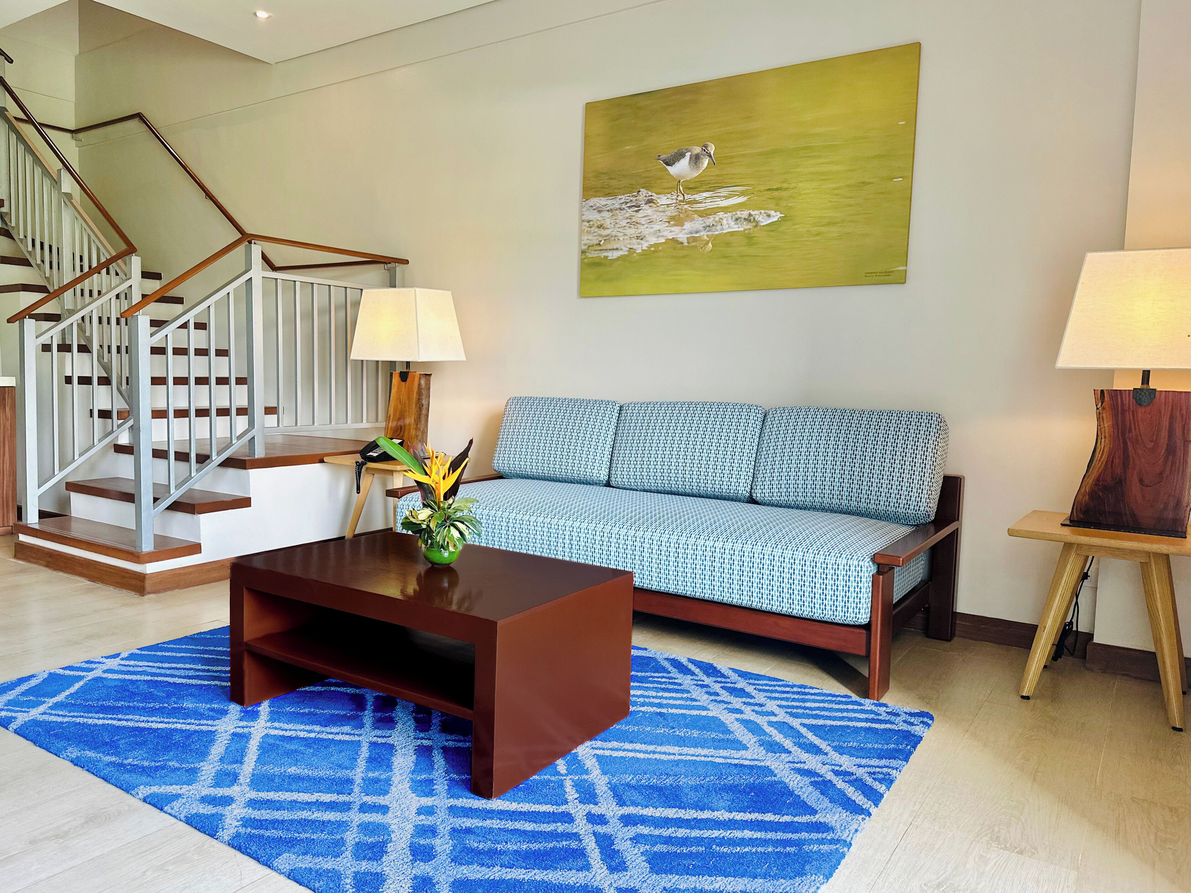 A modern living room with a staircase, a sofa, a coffee table, and a painting on the wall.