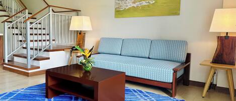 A modern living room with a staircase, a sofa, a coffee table, and a painting on the wall.