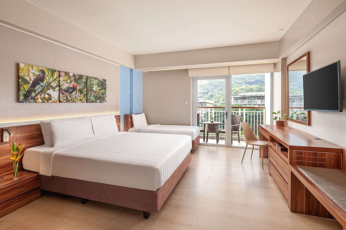 Ein modernes Hotelzimmer mit zwei Betten, einem Schreibtisch, einem Sessel, einem Fernseher und einem Balkon mit Bergblick.