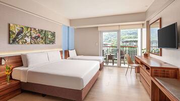 A modern hotel room with two beds, a desk, a chair, a TV, and a balcony with a view of the mountains.
