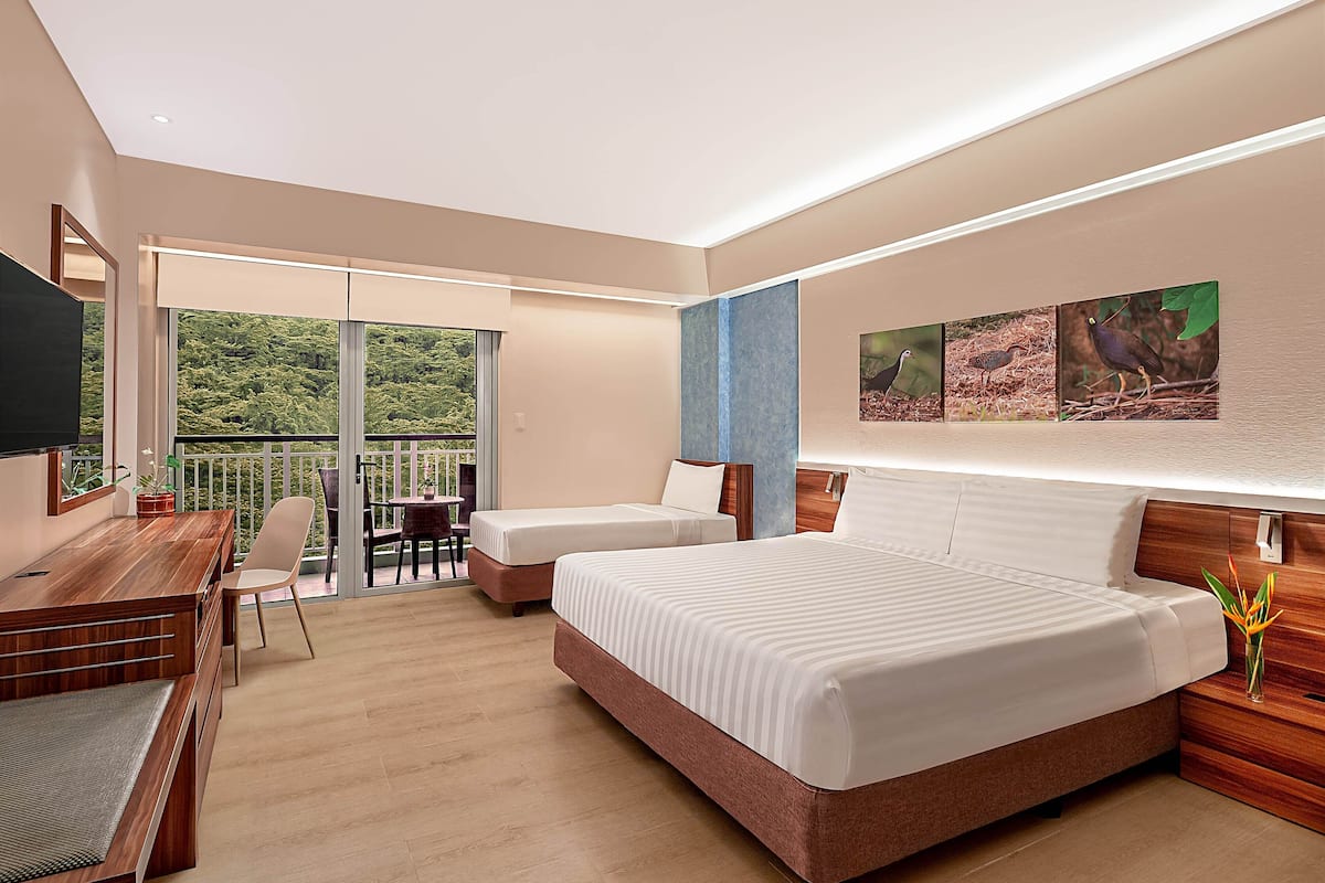 Ein modernes Hotelzimmer mit einem großen Bett, einem Schreibtisch mit Stuhl, einem kleinen Tisch und einem Balkon mit Blick auf Grünflächen.