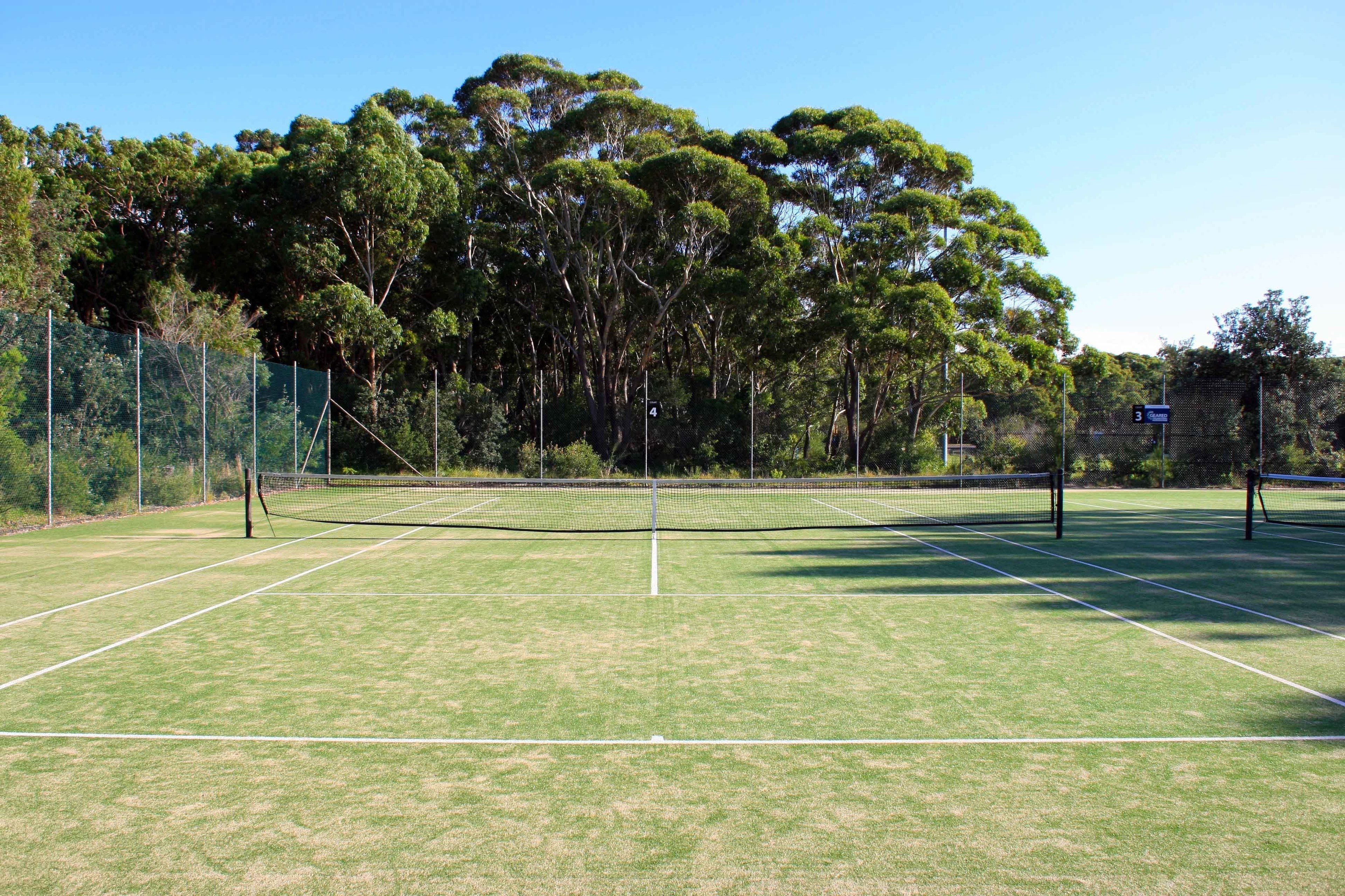 A tennis court with a net, surrounded by trees and a fence.