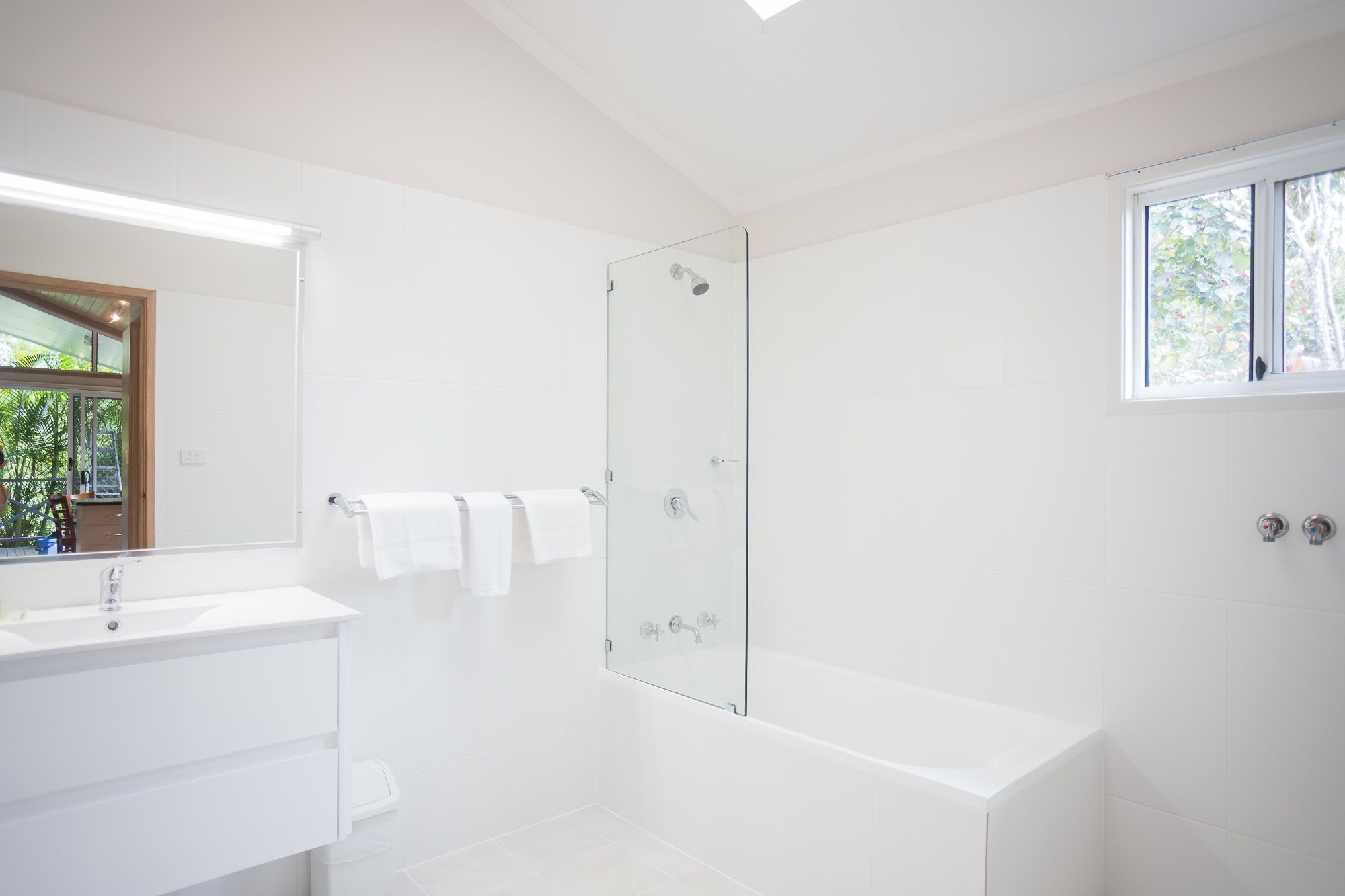 Un baño moderno con cabina de ducha de vidrio, una bañera blanca y un lavamanos con espejo.