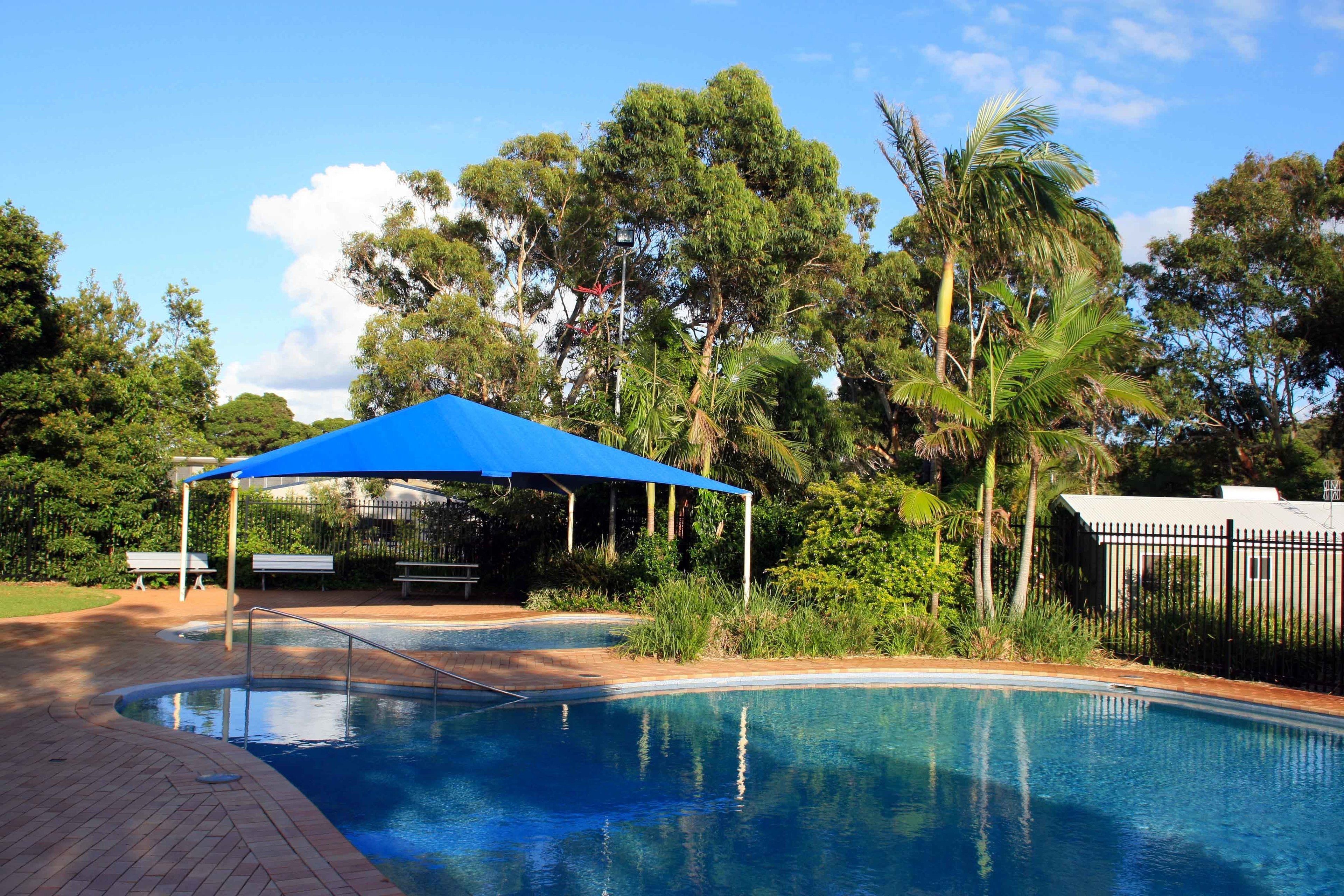 A swimming pool with a blue canopy, surrounded by lush greenery and trees.
