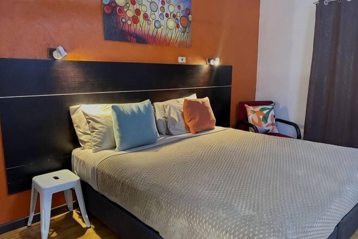 A bed with a headboard, pillows, a bedside table, and a wall-mounted light fixture.