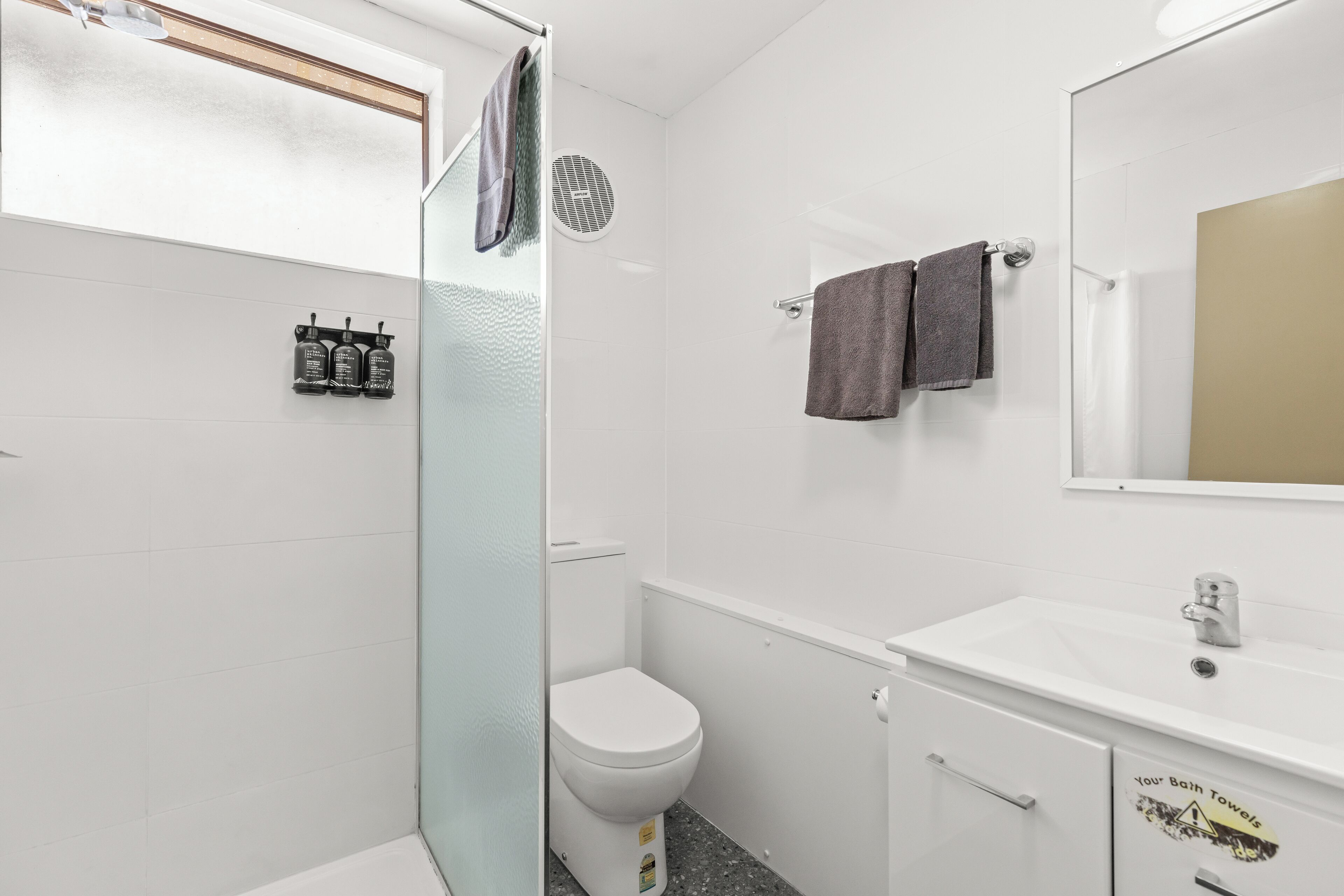 Un baño moderno con cabina de ducha de vidrio, inodoro blanco, lavabo con espejo y perchero con dos toallas.