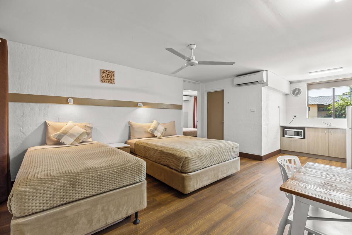 A hotel room with two beds, a ceiling fan, a kitchenette, and a view of the outside.