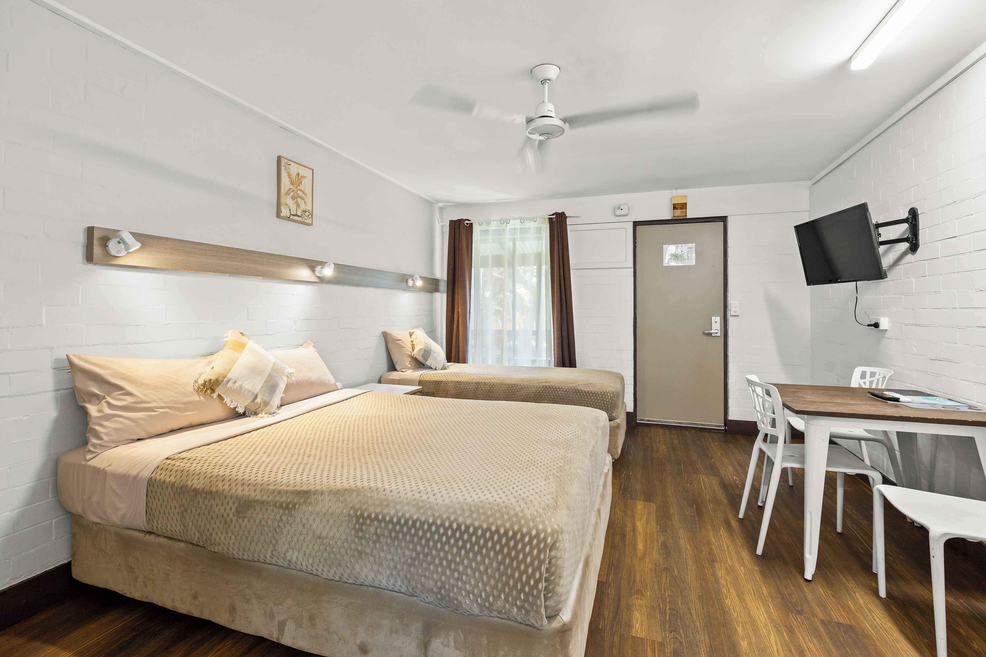 Habitación de hotel con dos camas, un escritorio, una silla, un televisor de pantalla plana y un ventilador de techo.