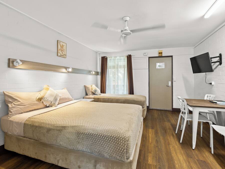 A hotel room with two beds, a desk, a chair, a flat-screen TV, and a ceiling fan.