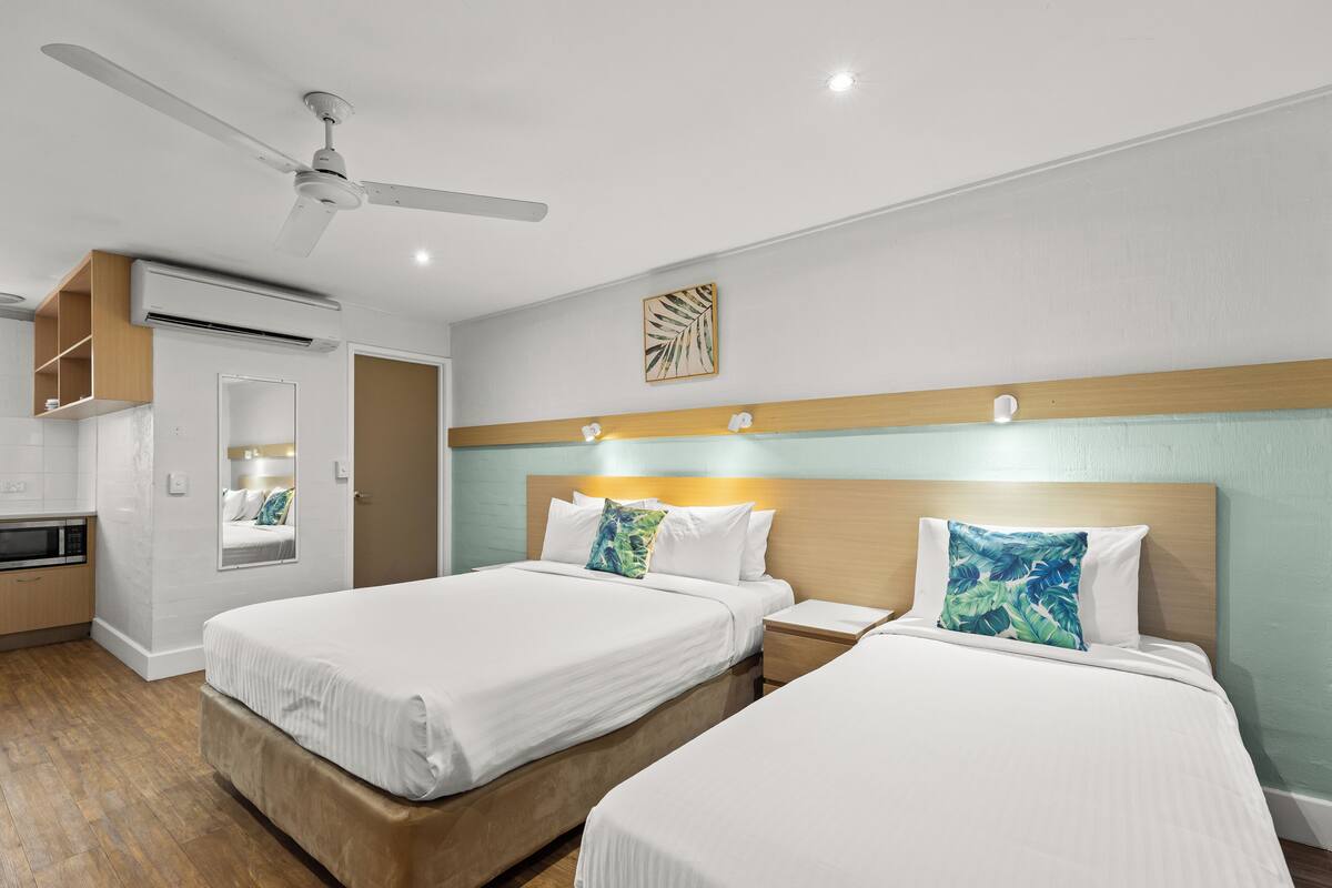 A hotel room with two beds, a ceiling fan, an air conditioning unit, a microwave, and a small kitchenette.