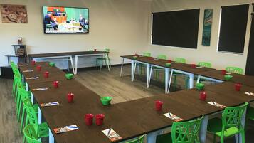 A conference room with multiple tables and chairs, a television screen displaying a news program, and a blackboard on the wall.