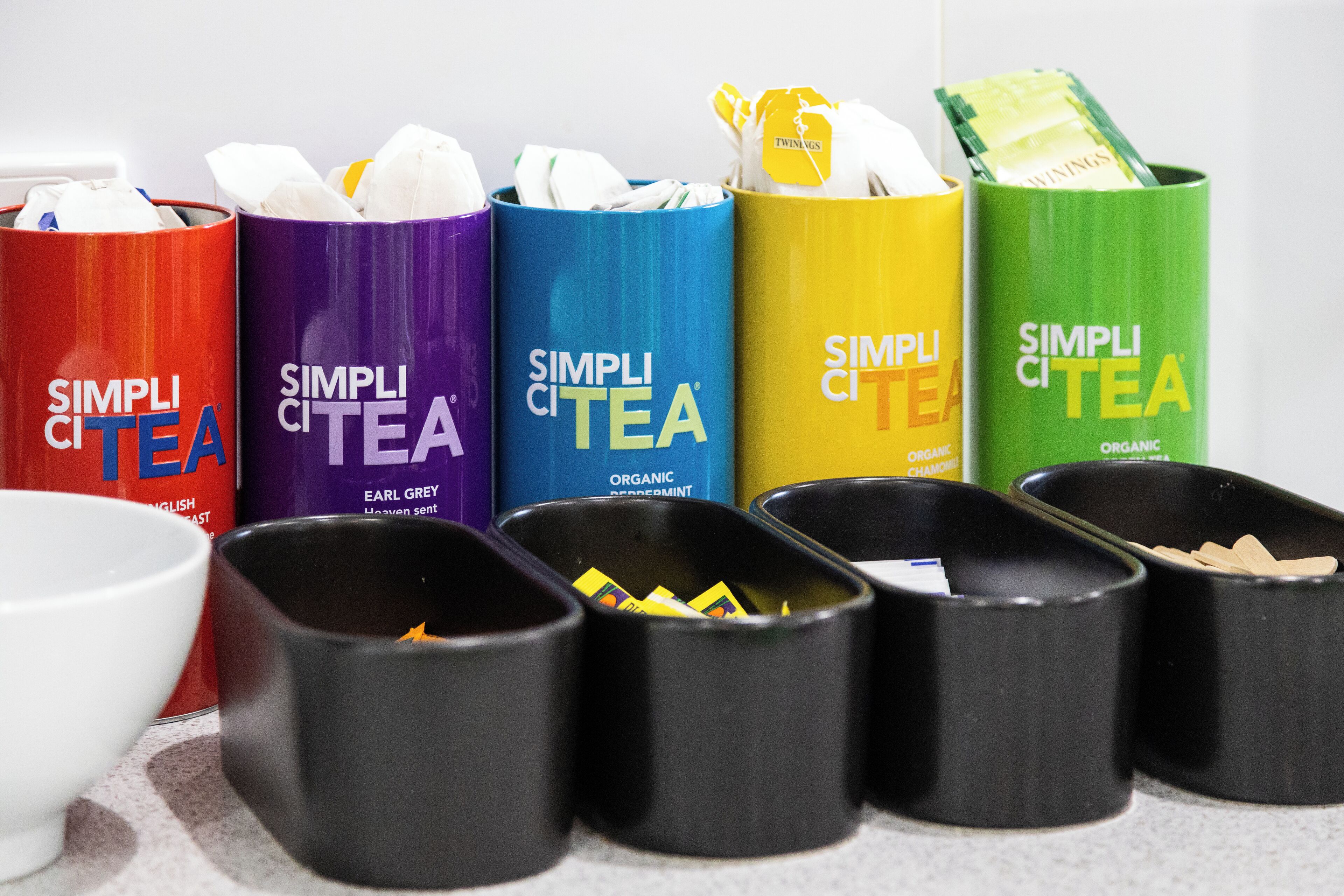 A row of colorful tea containers labeled 'SIMPLI CITEA' with different flavors.