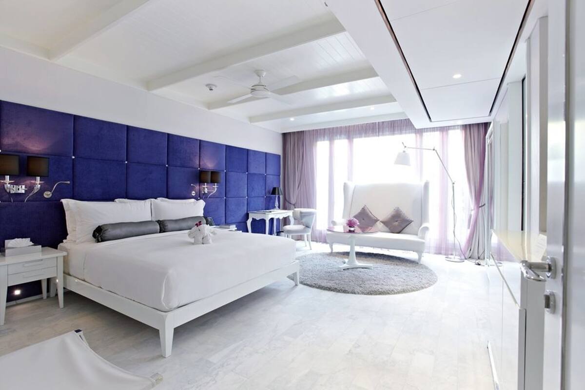 A modern hotel room with a large bed, a blue accent wall, a round seating area, and a view of the city.