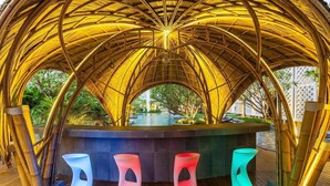 Un espacio al aire libre cubierto con piscina, estructuras de bambú y taburetes modernos.