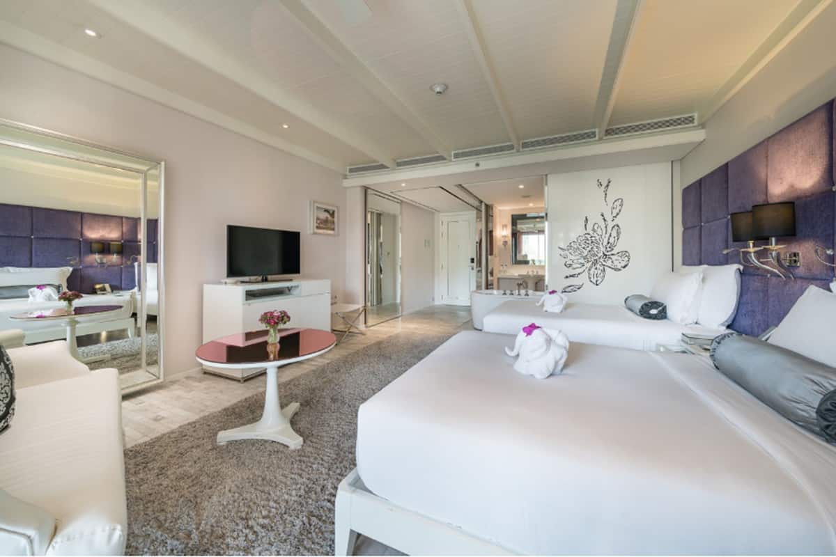 A modern hotel room with a large bed, a flat-screen TV, a seating area with a table, and a bathroom visible through an open door.