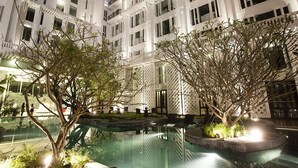 Un hotel de varios pisos con un patio que cuenta con una piscina, mobiliario exterior y árboles.