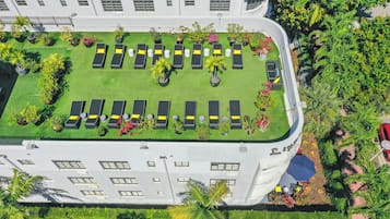 Vista aérea de um hotel com um jardim no terraço, várias cadeiras de descanso e área de piscina.