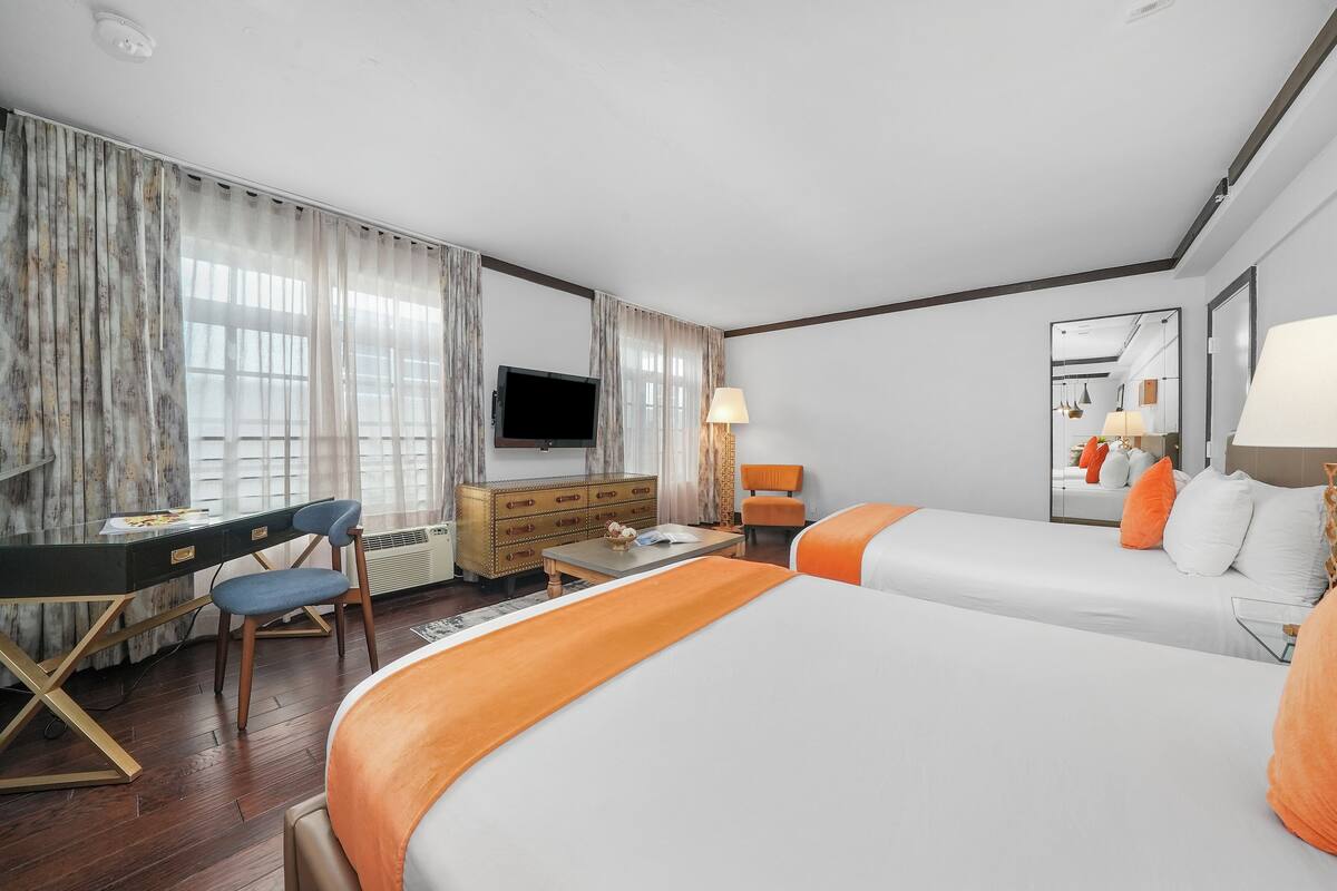 A hotel room with two beds, a desk, a dresser, a TV, and a mirror.