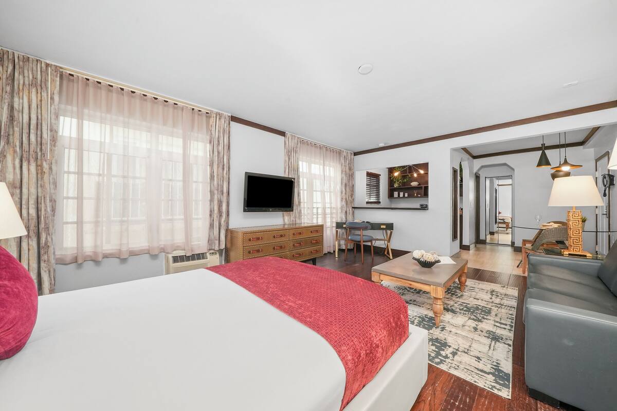 A hotel room with a bed, a desk, a chair, a TV, and a sofa.